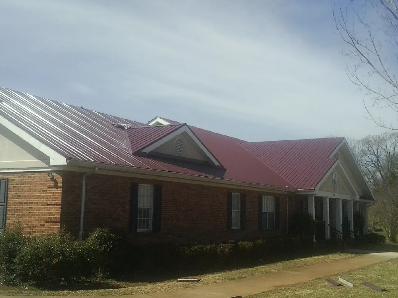 Red metal roof with gabled entries on a long brick building, from a Hail Damage Roof Repair job in Pendleton